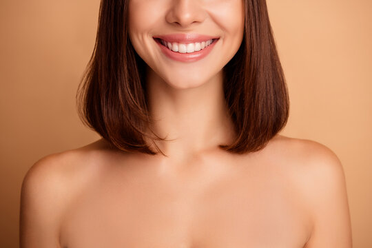 Smiling young woman with brunette bob shows natural makeup and glowing skin in a warm beige studio backdrop