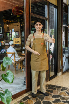 Portrait of young barista cafe owner standing at storefront with open sign, smiling confidently, representing independent entrepreneur lifestyle and sustainable small business startup growth concept