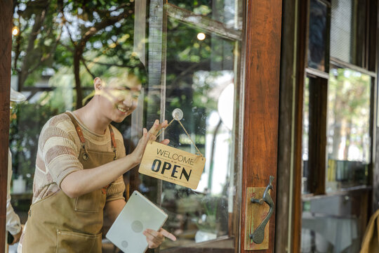 Young small business cafe owner placing closed sign on glass door, young entrepreneur ending daily service routine, reflecting on business operation and customer flow during quiet afternoon moment.
