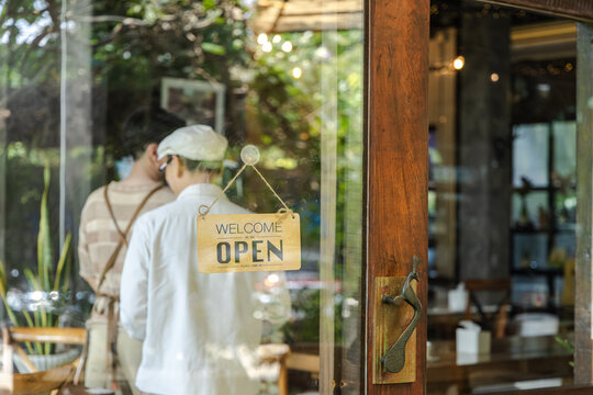 Small business startup, young cafe owner barista looking outside through door with closed sign reflecting concern about business situation and customer flow in coffee shop, worker flipped open sign