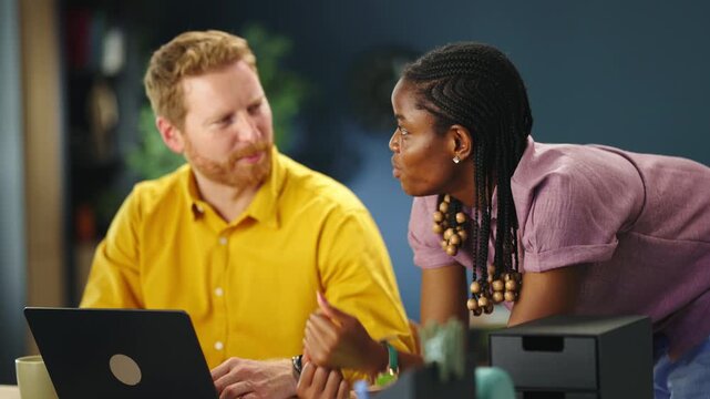 Two team members work together at a desk in an office. One person points at the screen while the other types. They discuss their thoughts on the task.