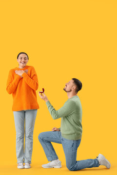 Young man proposing to his girlfriend on yellow background