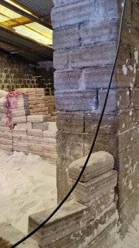Traditional salt processing workshop in Colchani near Salar de Uyuni, heaps of raw white minerals on floor and packaged blocks ready for distribution inside rustic adobe brick factory in Bolivia