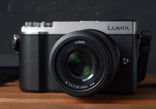 PERPIGNAN, FRANCE - MAY 12, 2026: A Panasonic Lumix GX9 mirrorless camera equipped with a Lumix G 25mm f1.7 ASPH lens on a wooden tabletop. A modern compact photography kit for street and portrait.