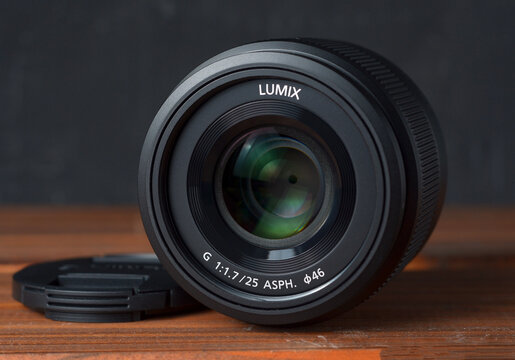 PERPIGNAN, FRANCE - MAY 12, 2026: A Panasonic Lumix G 25mm f1.7 ASPH (Model H-H025) mirrorless lens on a wooden surface. This fast prime lens is a popular choice for Micro Four Thirds system cameras.