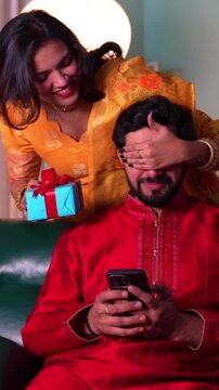 Young Indian couple in vibrant yellow traditional outfits celebrates diwali and shares a special moment with a surprise gift amid festive lights and flowers.