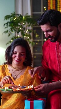 A happy young Indian couple in traditional attire light diyas in their beautifully decorated home filled with flowers and lights, creating cherished moments of joy