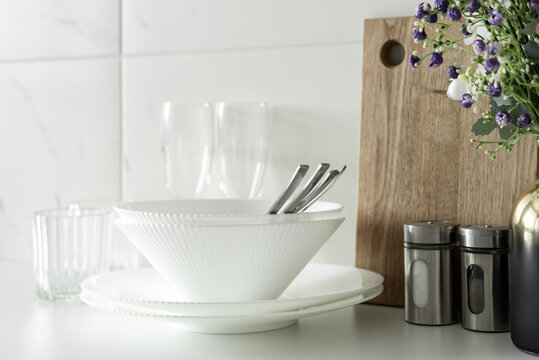 White bowls and plates with flowers and kitchen accessories in clean modern kitchen interior.