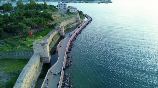 Aerial view of a historic stone fortress wall along the coastline with people walking. Turkey, Izmir, Eski Foca