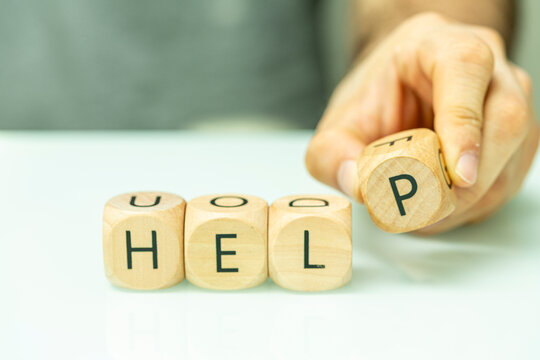 A close-up shot of a hand arranging wooden letter blocks to spell the word help.