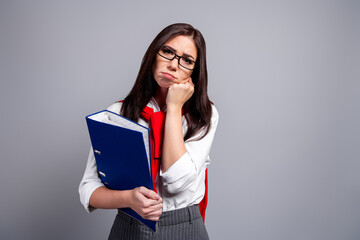 Fototapeta premium Bored student woman with glasses holding blue binder and paperwork, looking tired and frustrated while studying and dealing with documents