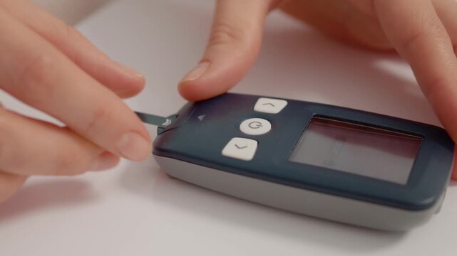A woman uses her hands to place a glucose strip into a glucometer to check her blood sugar levels. This action is part of her routine for managing diabetes.