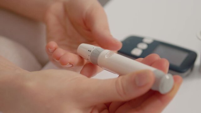 A woman holds a finger pricking device in her hands to check her blood sugar levels. She prepares to prick her finger for a glucose test to manage her health.