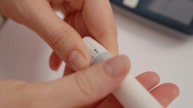 A woman prepares a finger pricking device before testing her blood sugar levels to monitor her health. She focuses on the process in a well-lit area.