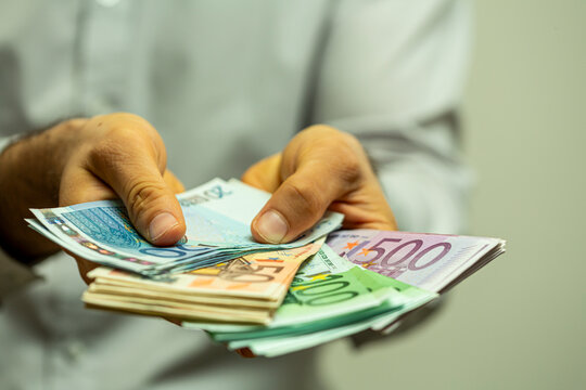 Close-up shot of a person's hands holding a large fan of euro currency notes