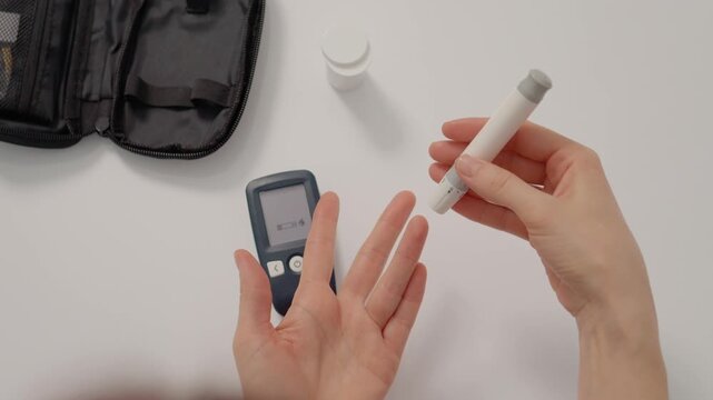 A woman uses a finger pricking device to check her blood sugar levels. She prepares the glucometer for testing at her kitchen table in a bright space.