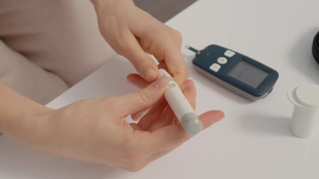 A woman uses a finger pricking device to check her blood sugar levels. She prepares to test her glucose and manage her diabetes health.