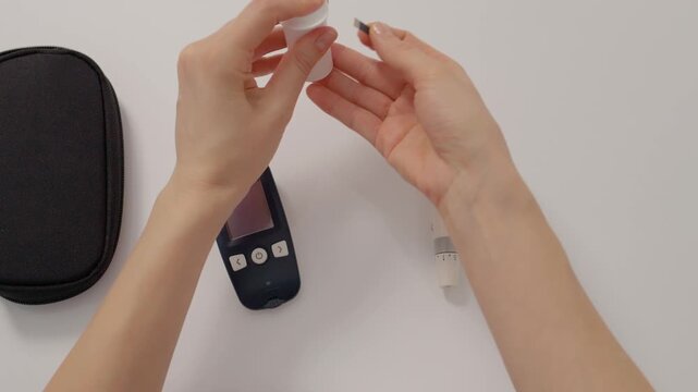 A woman prepares to test her blood sugar level at home. She inserts a strip into the glucometer to check her glucose level for diabetes management.