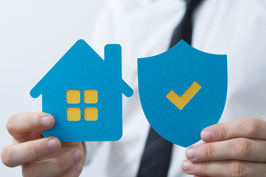 Business person holding a blue house and shield with checkmark for security