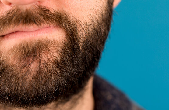 Close-up shot of a man's beard and face, showing texture and detail against a plain blue background.