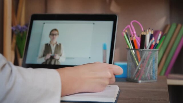 Woman taking notes during online lecture or webinar, remote work from home concept, female student studying with laptop, teacher on computer screen.
