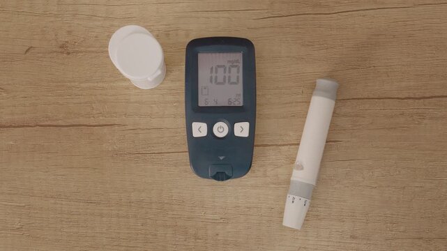 A glucometer sits on a wooden table showing a reading of 100 mg dL. This value is significant as it marks the line between diabetes and prediabetes.