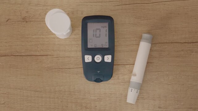 A glucometer shows a reading of 101 mg dL on a wooden table. This level is close to the limit between prediabetes and diabetes.
