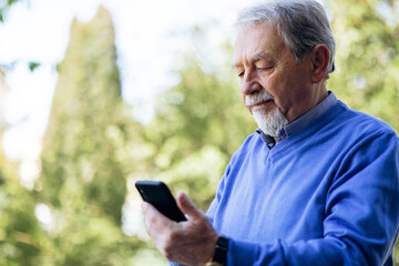 Obraz premium Elderly man with beard concentrating on smartphone outdoors, connecting with family and friends using mobile application