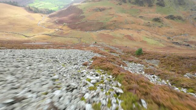 First person view flying down a mountain slope above a stone wall