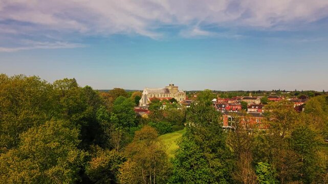 Drone aerial view across green trees toward Romsey Abbey and the surrounding historic town skyline in spring, Hampshire, England.