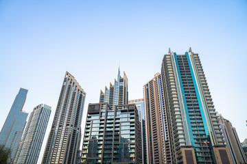 Fototapeta premium Modern skyscrapers rising in dense urban city skyline, tall glass buildings reflecting sunlight, metropolitan architecture, financial district, and contemporary city development concept.