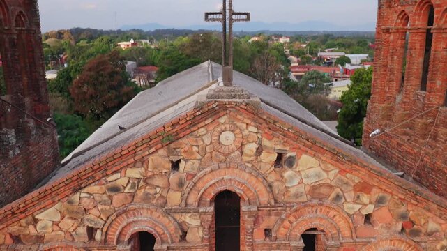 Framed aerial view of rooftop cross and twin towers, tilt down reveals facade of Nuestra Se&ntilde;ora de Asuncion historical church in Villarrica, Paraguay