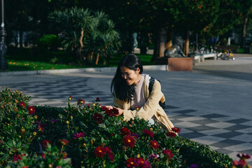 Obraz premium Woman in a yellow dress tends vibrant flowers in a city park, sunlight filtering through trees, a serene outdoor gardening moment, colorful fragrance, and floral beauty