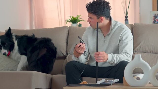 frustrated young man trying to understand difficult home product assembly instructions while his loyal border collie dog sits nearby on the sofa in a cozy modern living room setup