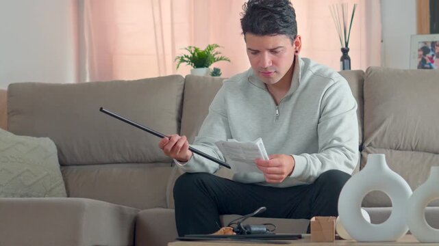 focused young man sitting on a sofa and looking confused while trying to decipher complex assembly instructions for a new home product in a cozy living room setting