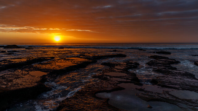 Aerial view of Hartenbos coastline with a golden sunset over the ocean, rocky tide pools reflecting the sky, and gentle waves Mossel Bay, Western Cape, South Africa.