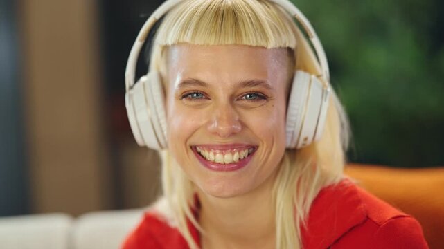 A person sits on a couch wearing headphones. They listen to music, closing their eyes. The setting is a cozy room with plants. The focus is on the person's relaxed expression.