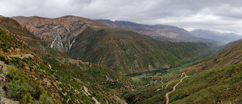 Aerial view of Die Hel Gamkaskloof valley with a winding road, rugged mountain peaks and greenery in Central Karoo District Municipality, Western Cape, South Africa.