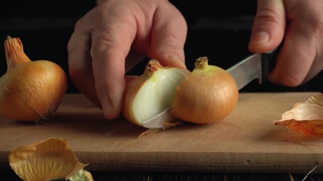 Close-up of hands slicing an onion with a sharp knife on a wooden cutting board, showcasing the peeling process and revealing the inner layers