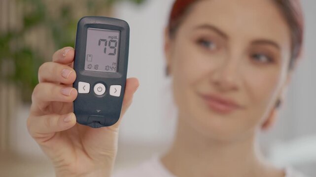 A woman shows a glucometer reading of 79 mg dL, which indicates good blood sugar levels. She demonstrates the importance of monitoring glucose for diabetes care.