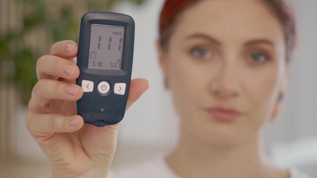 A woman displays her glucometer to the camera, showing a reading of 111 mg dL. She talks about blood sugar levels and their importance for health.