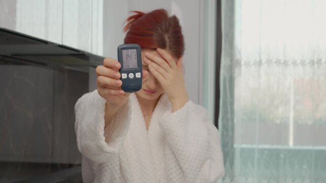 A woman in a kitchen displays a glucometer reading of 141 mg dL. This indicates a high blood sugar level, relevant for those monitoring diabetes.