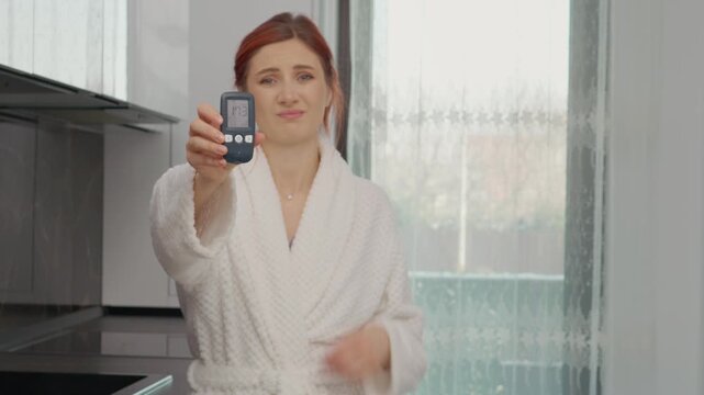 A woman in a kitchen checks her glucometer reading which shows 173 mg dL. She looks concerned about her high blood sugar level and takes notes.