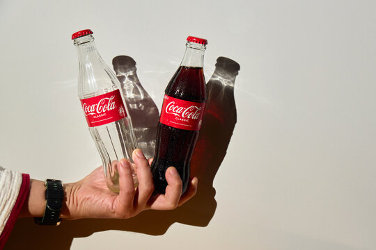 Tyumen, Russia-April 20, 2026: Hand holding empty and full glass Coca-Cola bottles with sharp shadows