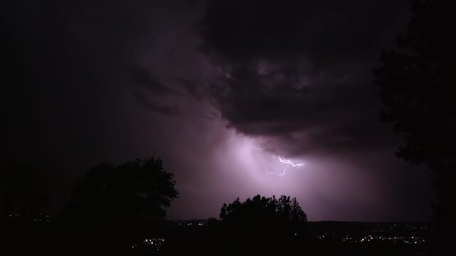 Lightning strikes on a dark night sky over a city landscape, captured in slow motion.