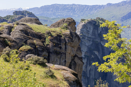 stunning aerial view of the majestic meteora sandstone rock formations in greece under a clear blue sky, featuring lush greenery and distant snow-capped mountains.