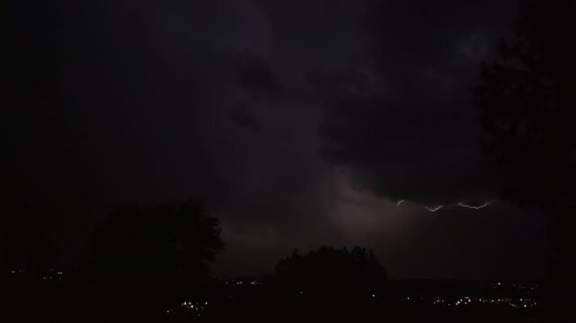 Lightning strikes on a dark night sky over a city landscape, captured in slow motion.