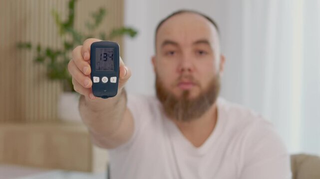 A man holds a glucometer with a reading of 134 mg dL. This reading shows a high blood sugar level. He looks concerned about his health and the implications of diabetes.