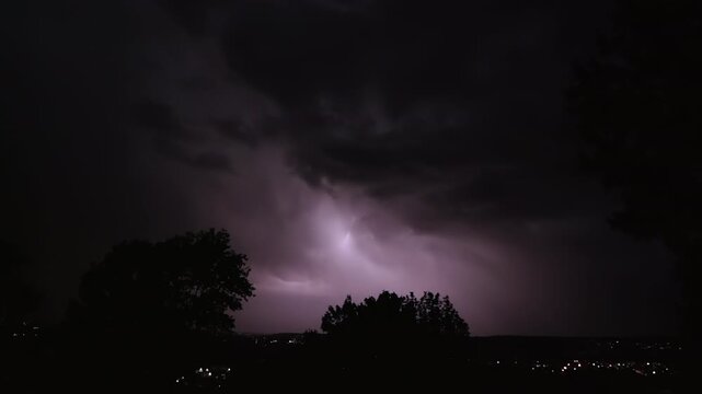 Lightning strikes on a dark night sky over a city landscape, captured in slow motion.