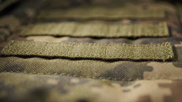 Close-up of camouflage fabric texture. Fabric appears slightly wrinkled. Background is blurred, focusing on material details.